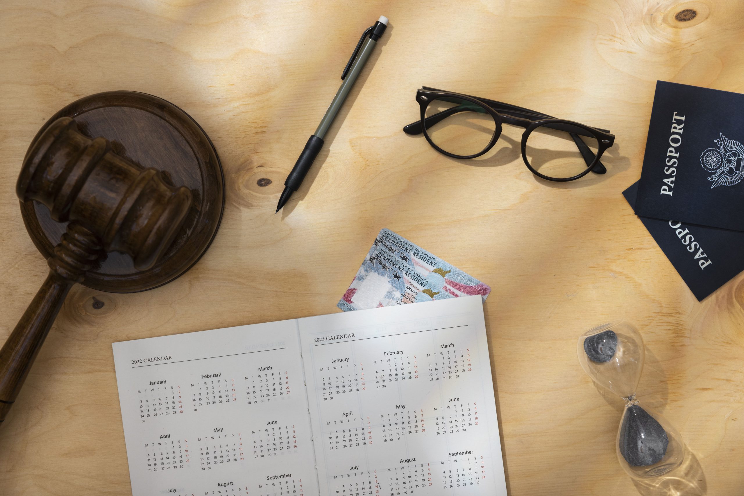 un calendario junto con un martillo que representa las leyes, unas gafas, unos pasaportes y un lapicero