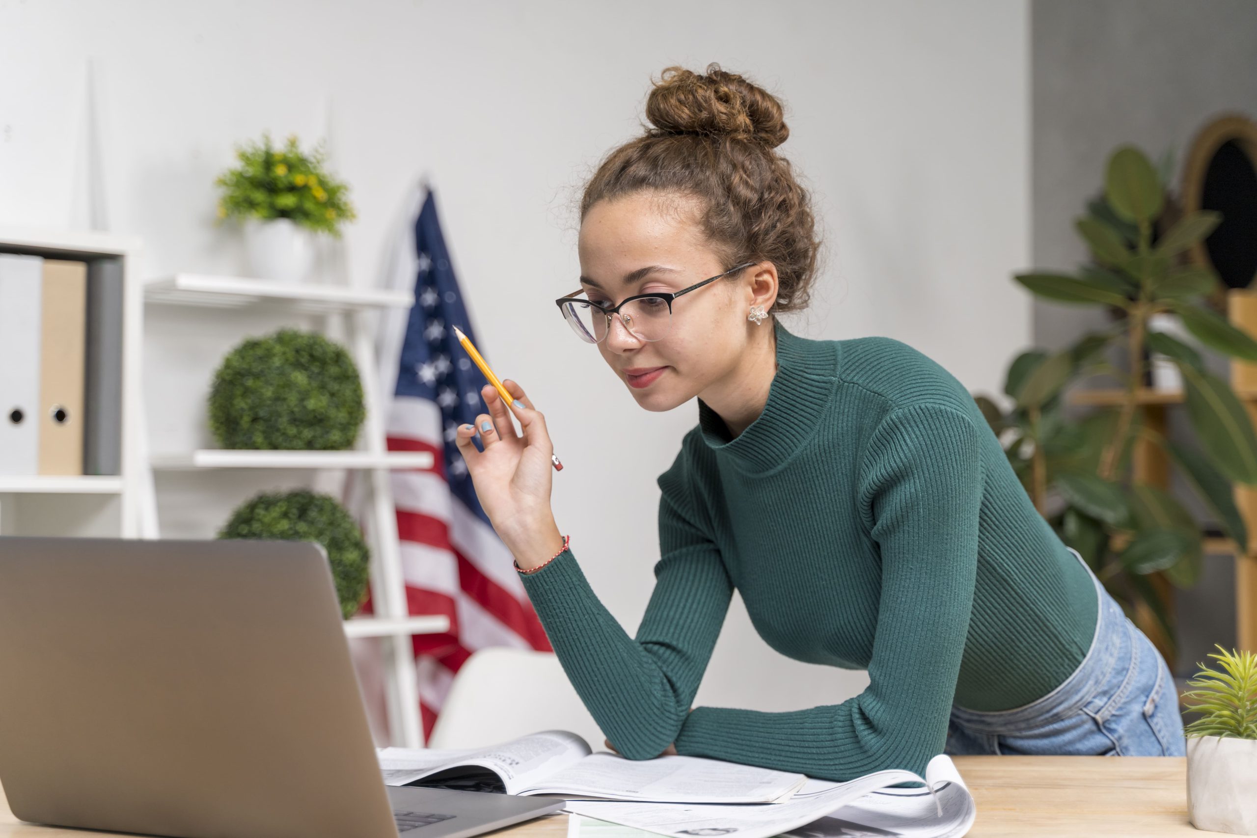 una mujer mirando a la pantalla de un computador, de fondo se ve una oficina y una bandera de estados unidos