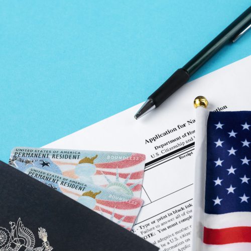 un pasaporte con dos greencard de estados unidos junto a una bandera del mismo pais y un formulario de visa